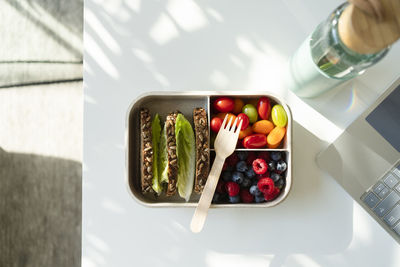 Rye bread, berries and salad with disposable fork in lunch box on table