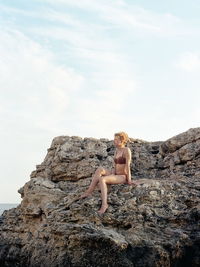 Low angle view of woman sitting on rock formation against sky