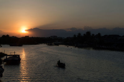 Silhouette of boat sailing in river during sunset