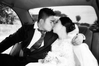 Bride and groom kissing while sitting in car