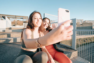 Smiling females friends taking selfie sitting outdoors