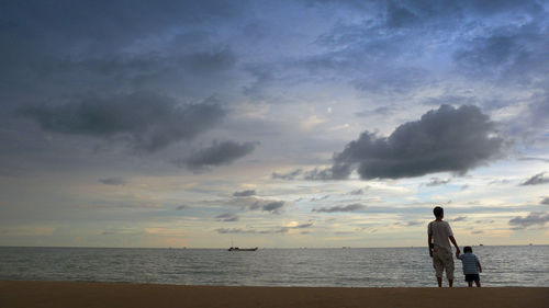 Rear view of men standing at beach against sky