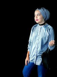 Portrait of young woman standing against black background