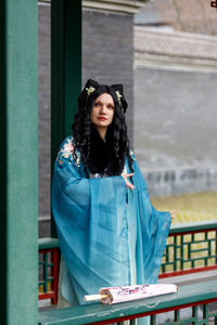 Portrait of young woman standing against building