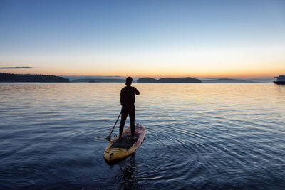 Rear view of man in sea against sky during sunset