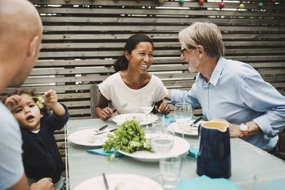 Happy senior man talking to daughter-in-law at outdoor dining table