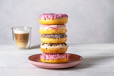 Glazed donuts on plates and coffee latte or cappuccino with milk foam in a heat-resistant glass cup