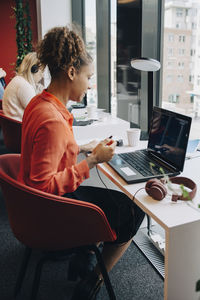 Side view of businesswoman using laptop while sitting at desk in office