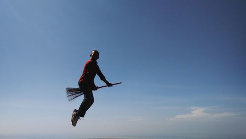 Low angle view of a man flying on broom against sky
