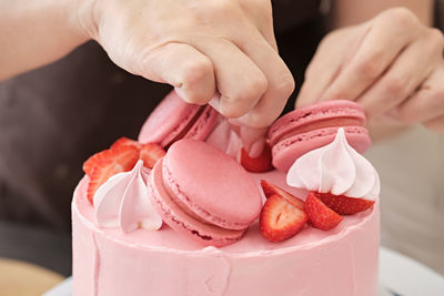 Woman pastry chef decorates pink cake with macaroons and berries, close-up. cake making process