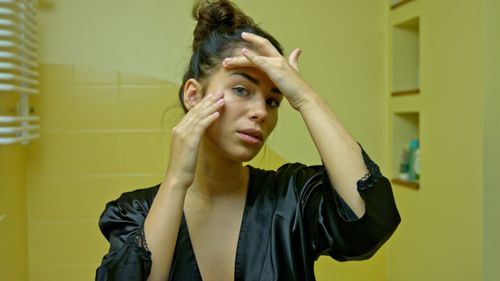 Portrait of young woman standing against yellow wall