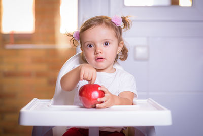 Cute baby girl with fruit on high chair at home