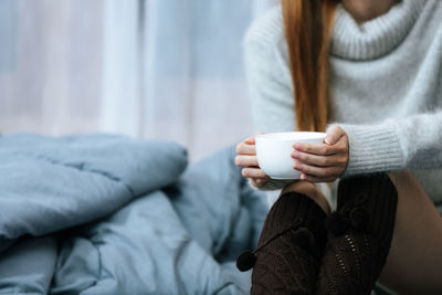 Low section of woman sitting on bed at home