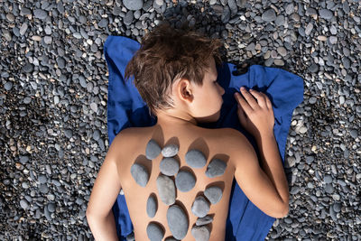 The boy lies on a pebble beach. stone therapy. relaxation, kids mental health. relax. sun.