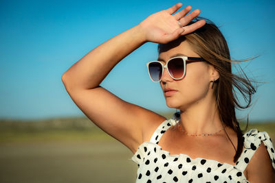 Portrait of young woman wearing sunglasses against clear blue sky