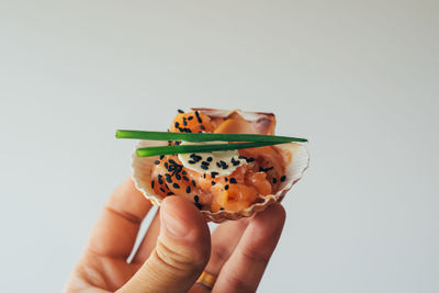 Cropped image of person holding cured salmon in seashell against white background