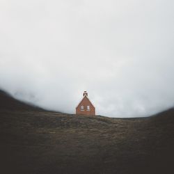 Cross on land by building against sky