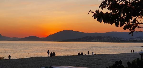 Silhouette people on beach against sky during sunset