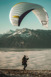 Person paragliding over mountains against sky