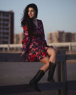 Portrait of beautiful young woman sitting on railing