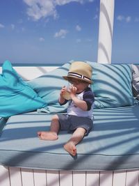 Baby drinking from glass while sitting on seat against sky