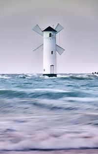 Lighthouse by sea against clear sky