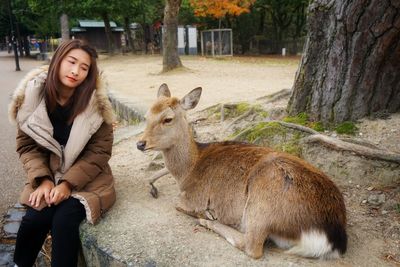 Woman looking at deer sitting by tree