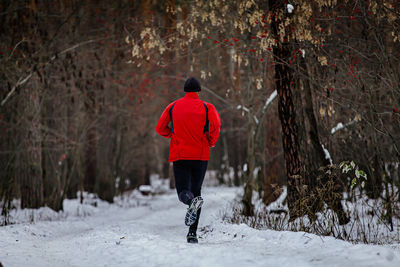 Rear view of man walking on snow covered field