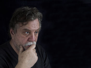 Close-up of worried mature man against black background