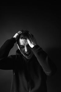 Young man screaming against black background