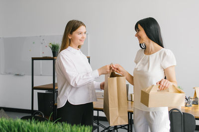 Two girls are working in an office at a desk with a laptop and a craft package