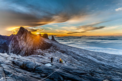 People on snowcapped mountain against sky during sunset