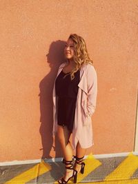 Portrait of smiling young woman standing against wall