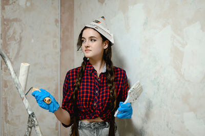 Portrait of young woman standing against wall.  painter works occupation 