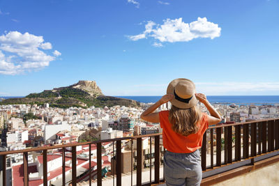 Tourist holding hat and looking at alicante and mount benacantil with santa barbara castle, spain