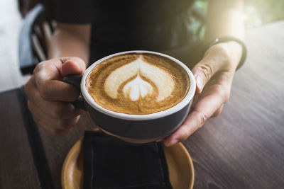 Midsection of woman holding coffee cup on table
