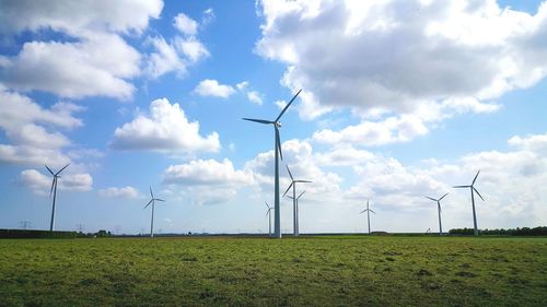 Windmills on grassy field against sky