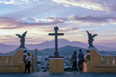 Rear view of man and woman standing statue against sky during sunset