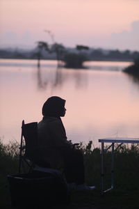 Rear view of silhouette man looking at lake during sunset