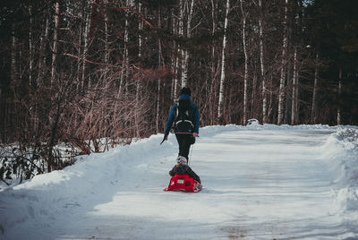 Rear view of woman with son walking on snow covered road