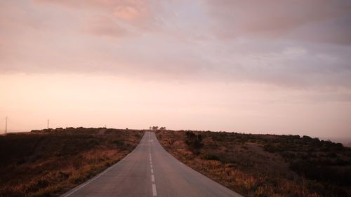 Empty road along landscape against cloudy sky