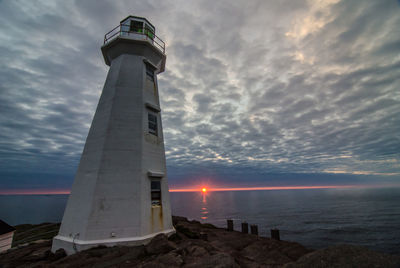 Low angle view of lighthouse by sea against cloudy sky during sunrise
