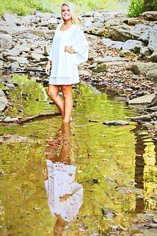 PORTRAIT OF YOUNG WOMAN STANDING BY WATER