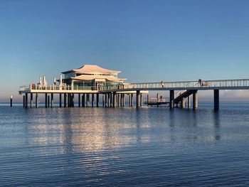 Pier on sea against clear blue sky