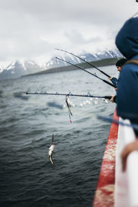 People fishing while traveling in boat on sea against sky