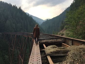 Rear view of woman walking on bridge edge against mountains