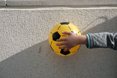 High angle view of person holding ball on yellow wall