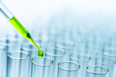 Close-up of green liquid pouring from pipette in test tubes