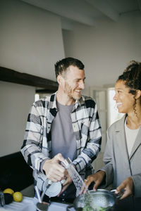 Cheerful multiracial friends washing dishes together in sink at home