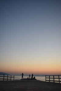 Silhouette people on beach against clear sky during sunset